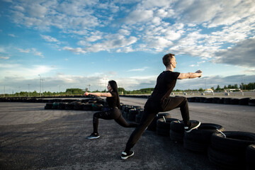 Fototapeta na wymiar Man and woman making lunges on a sunny morning outdoors using tires.