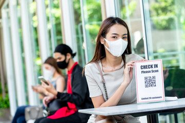 Cute teenage woman wear mask show sigh with text 'check in please scan' and QR code for customer to check in before enter a restaurant, application for covid-19 situation quarantine