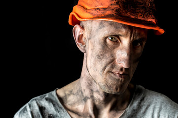 The face of a male miner in a helmet on a black background.