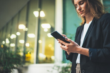 Closeup of female hands using modern smartphone device near urban office, focus on cellphone,...