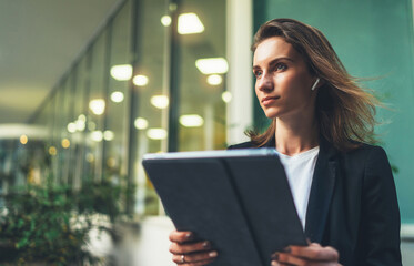 side view of an elegant girl in a business black suit holding a tablet and reading correspondence,  financial adviser uses Internet technology on computer near office