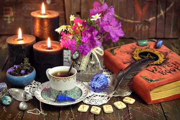 Romantic still life with cup of tea, witch book, runes and black candles.