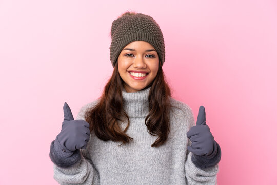 Young Colombian girl with winter hat over isolated pink wall giving a thumbs up gesture