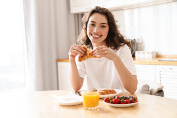 Photo of woman smiling and eating croissant while having breakfast