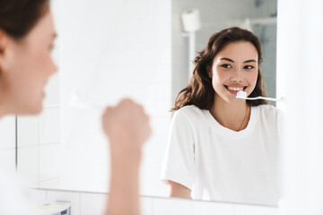 Photo of cheerful woman cleaning teethes while looking at mirror