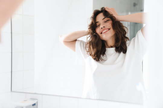 Photo of smiling woman grabbing her head while looking at mirror