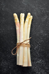 Raw white fresh asparagus on a black stone background. Healthy food. Top view. Free space for your text.