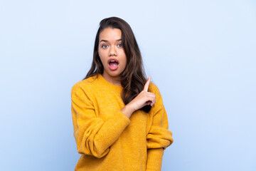 Fototapeta premium Young Colombian girl with sweater over isolated blue background surprised and pointing side
