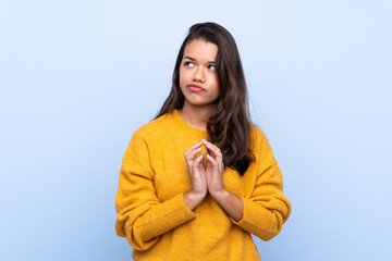 Young Colombian girl with sweater over isolated blue background scheming something