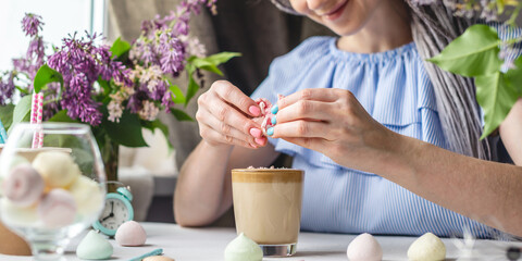 Young cheerful woman is breaking meringue and sprinkles delicious whipped coffee on top. A nice morning coffee on a sunny summer day