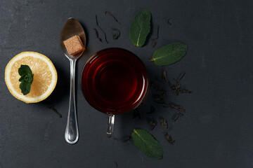 Glass cup of tea with mint leaves and lemon on a dark background Top view. Copy space.