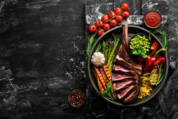 Grilled steak on the bone with grilled vegetables. On a black background. Top view. Free copy space.