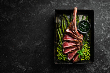 Tomahawk steak on the bone. Grilled steak with asparagus and green peas. On a black background. Top...