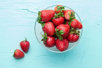 Fresh strawberries in a glass plate on a blue background. Summer berries. View from above