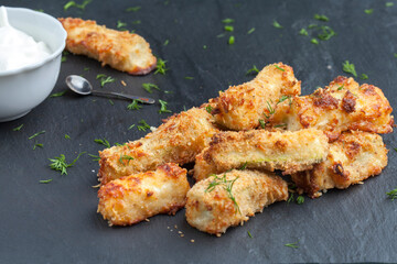 Zucchini baked with parmesan cheese and herbs on a black background. Appetizing zucchini in the form of sticks. Vegetarian cuisine. Vegetable course.