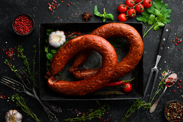 Rings of traditional smoked sausage in a country style composition. on a black stone background....