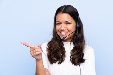 Young telemarketer Colombian woman over isolated blue background pointing finger to the side - obrazy, fototapety, plakaty
