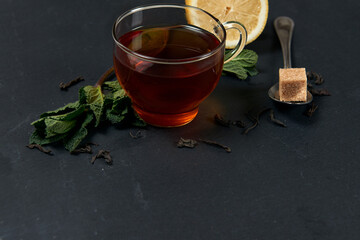 Glass cup of tea with mint leaves and lemon on a dark background. Copy space