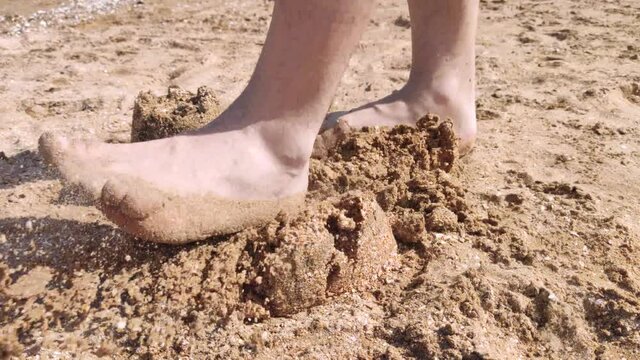 A father walks along the beach and steps on sand castles that his child built. The concept of child abuse, suffering and destruction of dreams. Family problems