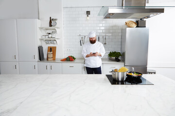 Experienced male chef cook standing on big modern kitchen while using smart phone