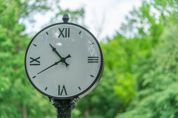 big white street clock on a background of green trees