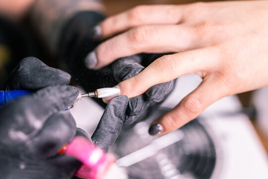 Close-up of manicurist woman removes gel shellac polish from client's nails using manicure machine. Manicure master is working with electric nail drill in beauty salon. Hardware manicure process.