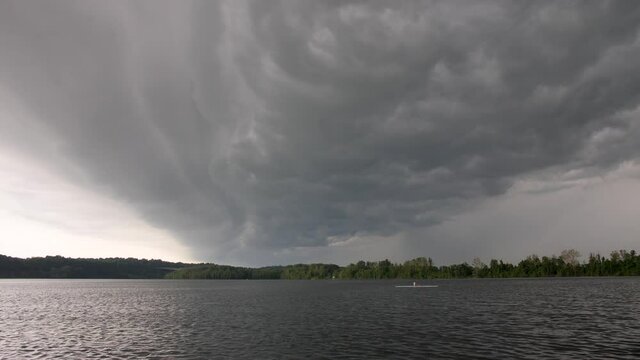 Big storm clouds billowing and rolling across frame as a single rower goes across this midwestern urban lake.
