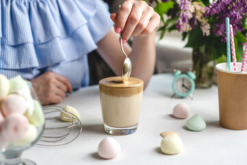 Woman is picking up a spoon and gently stirs the thick whipped mousse in a glass of cold coffee. Gentle atmosphere and sunny beautiful summer morning