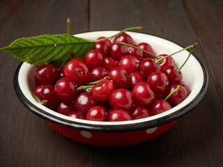 Fototapeta na wymiar ripe red cherry in a round metal bowl on a brown wooden background
