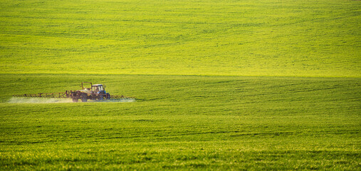 Tractor spraying pesticides on field with sprayer at summer