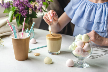 Woman is picking up a spoon and gently stirs the thick whipped mousse in a glass of cold coffee. Gentle atmosphere and sunny beautiful summer morning