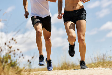 Young athletic couple running around field under sunlight. Only body, no face