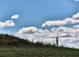Fit athlete woman running down a field hill. Outline of a hill