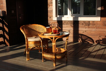 Chair and table patio in the rays of the evening sun. Jar of dandeloin jam, cup of tea and basket of dandelion flowers