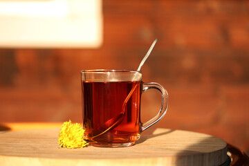 Glass Tea Mug with Spoon and dandelion flower on the wooden table in the garden