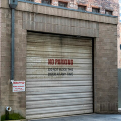 Square crop Corrugated metal garage door of an old brick building with No Parking sign