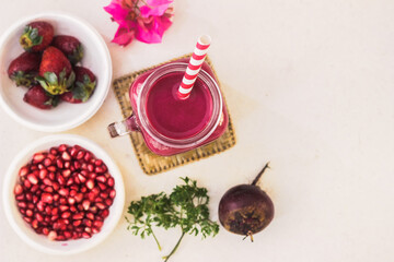 Red Juice in Mason Jar with paper straw on a white background surrounded by Beetroot, Pomegranate Seeds and Strawberries. Healthy Living Concept.