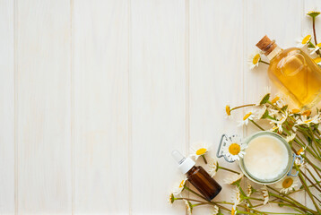Chamomile flowers and cosmetic bottles of essential oil and extract on white wooden background. Flat lay. Top view. Copy space
