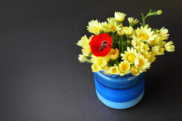 Yellow daisies and single red Poppy flower in a rustic blue pot against dark gray background. Simple romantic lovely bouquet of a wild flowers. Copy space. Greetings, gift