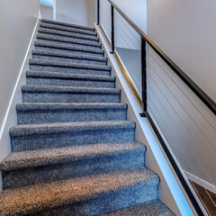 Square Indoor stairs of home with metal handrail and gray carpet on the treads