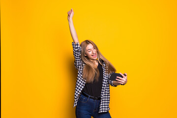 Portrait of a cheerful young woman holding mobile phone, celebrating standing isolated over yellow background