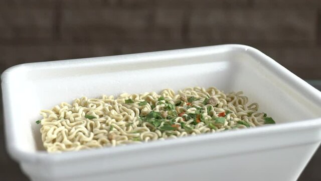 Instant noodles with spices are poured with hot water. Ramen in a plastic plate. Drops splash in different directions. Slow motion