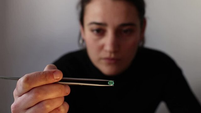 Female gemologist looking at an emerald gemstone clamped with jewelry tweezers