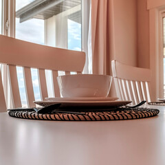 Square Tableware and utensils on woven placemat at the dining table with chairs