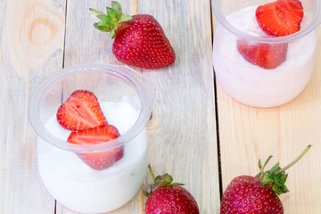 Sliced ​​strawberries in half, jars of yogurt on a wooden table