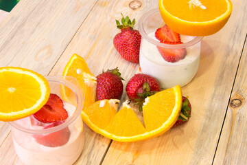 Sliced ​​strawberries in half, orange sliced ​​jars of yogurt on a wooden table
