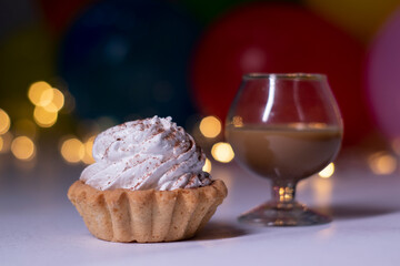 festive cupcake and a glass with a brown liquid - liquer. On the background of multi-colored balloons and lights. party, birthday concept. Copy space. High quality photo