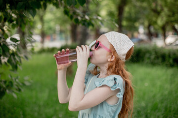Red-haired child drinks water from a plastic bottle