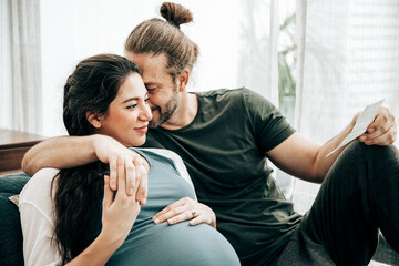 Pregnant women and handsome husband lying and analyze the ultrasound film of the fetus. He takes care of her closely with love and cherish, with gladness and successful. Being maternity and parenthood