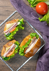 Delicious croissants sandwichs with fresh Ham, cheese, tomato, cucumber, lettuce and Sub sandwich with fresh salad, Ham , cheese served on sieve. wooden background Top view. Flat lay.